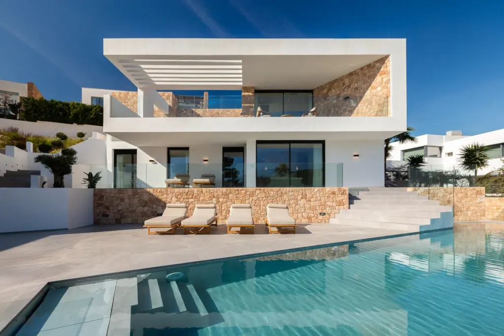 Situada en el corazón de Cap Martinet, en Santa Eulalia del Río, CASA CM se erige como una respuesta clara y contundente a la topografía del terreno. Lejos de seguir la pendiente de manera escalonada, la vivienda atraviesa el paisaje, insertándose parcialmente en la ladera mientras, a su vez, emerge sobre ella, estableciendo un diálogo sutil pero fuerte entre la geometría y la naturaleza.